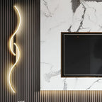 Aveloro Ondula Wellen-Wandleuchte in Gold neben einem Fernseher